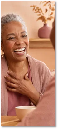 An older woman laughing over a cup of tea