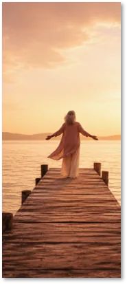 A woman at the end of a jetty at sunset, arms open
